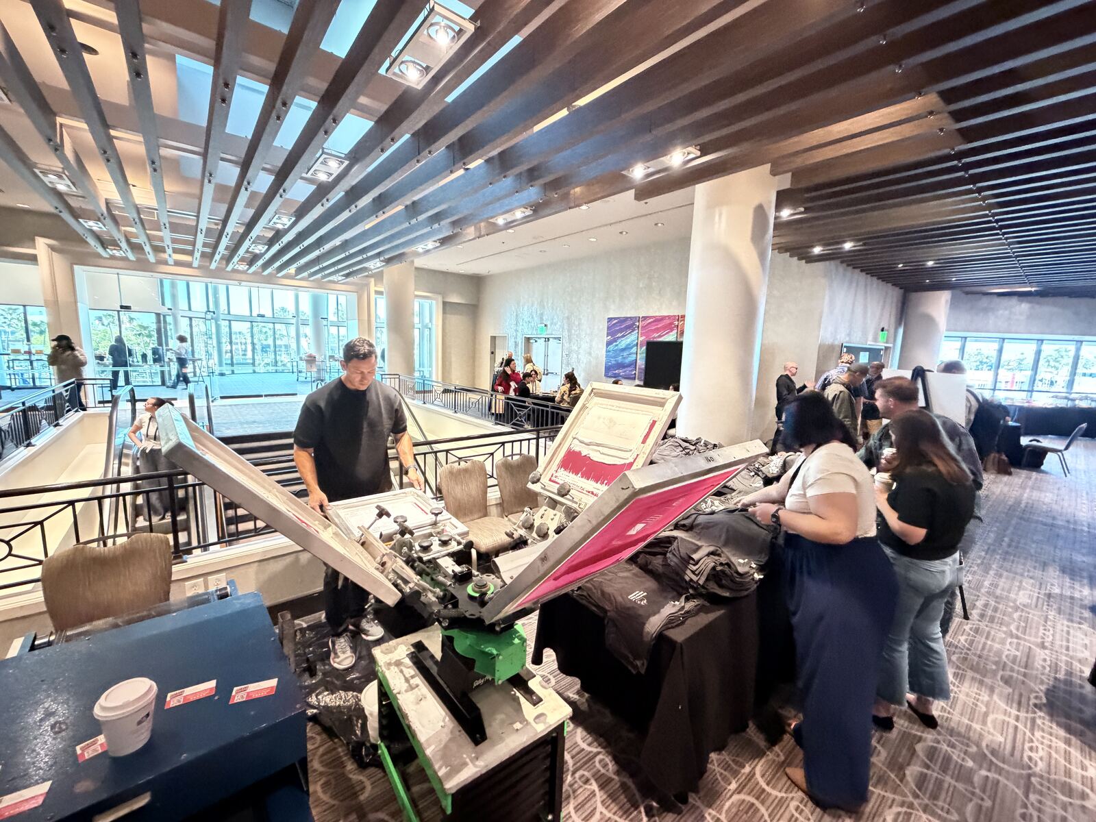 Live screen printing demonstration booth at an event with decorated apparel samples displayed and an operator working at the press