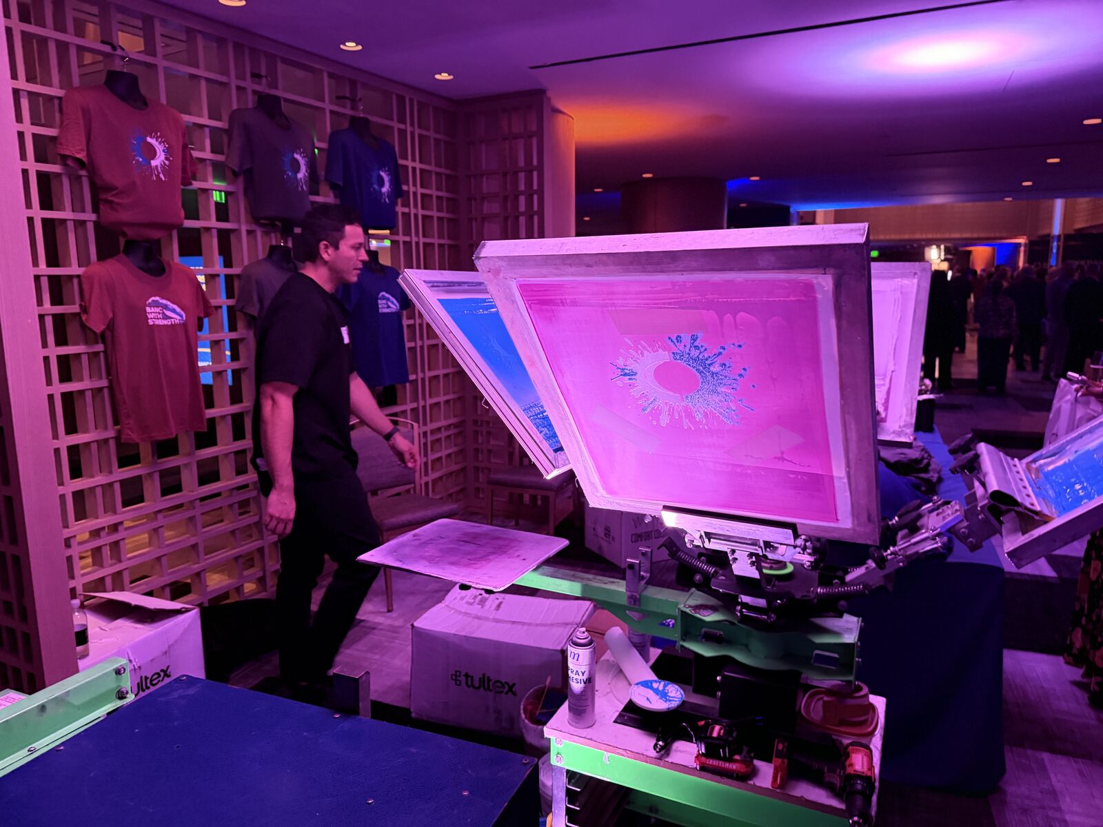 Professional demonstration of UV DTF and heat press equipment at a branded booth with an operator showing printing capability